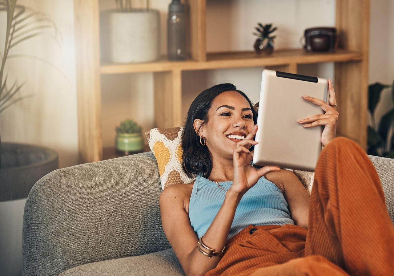 A woman is lying on a couch and using a tablet to research brand awareness.